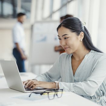 A professional woman logs into her Patelco Online account on her laptop at work.