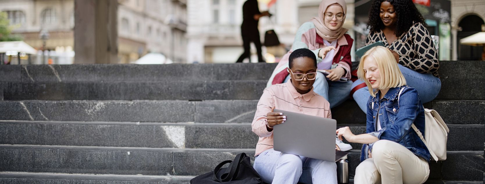 A diverse group of college women sit on outdoor stairs on campus.