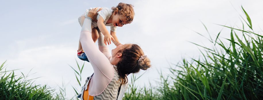 A young mom holds her giggling baby up in the air.