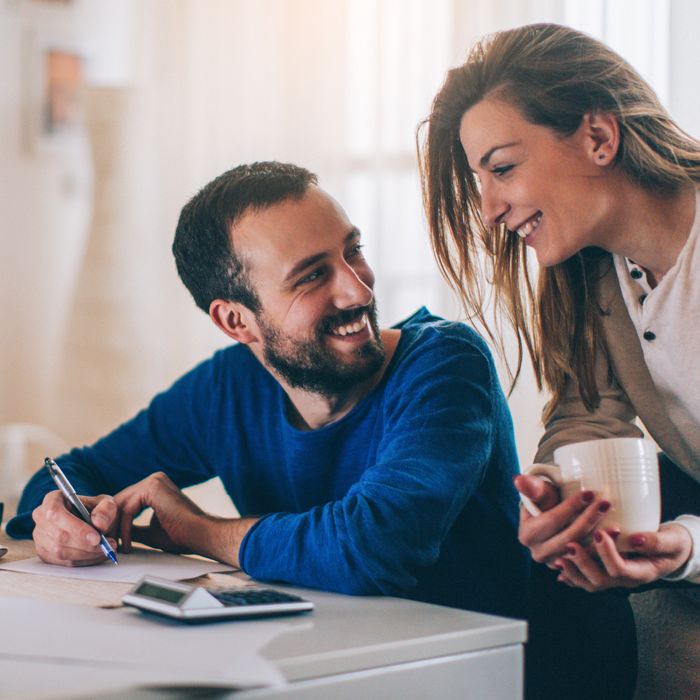 A young couple smiling over the kitchen table using the Patelco Mobile App on their phone