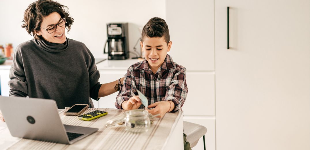 A smiling mom pats her son on the back while they talk about budgeting and savings.