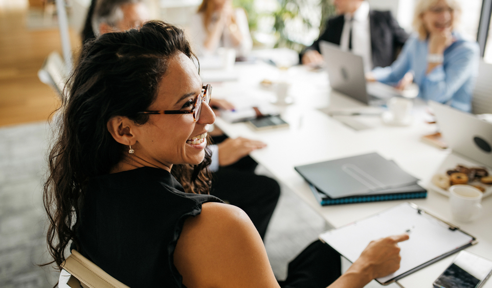 A woman smiles with her coworkers at a conference table.