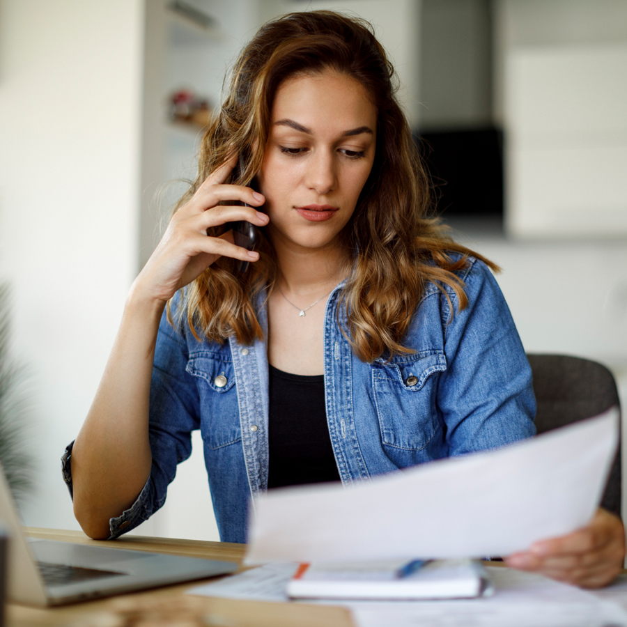 Patelco member at the kitchen table holding up a mobile device and looking at a bill.